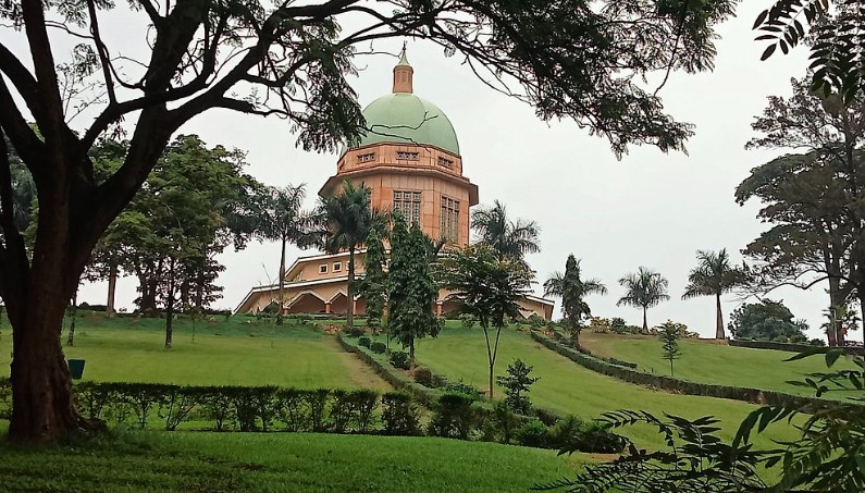 Lush gardens surrounding the Bahá'í Temple in Kampala, with vibrant flowers, tall trees, and a peaceful walking path, offering a tranquil escape for visitors.