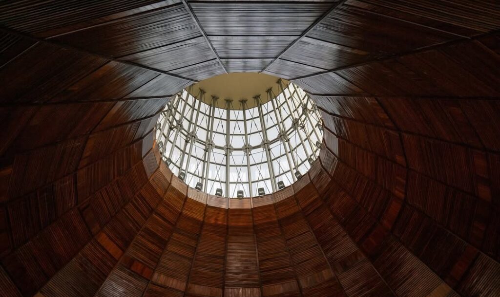 Interior of the dome, showcasing its pale blue ceiling, circular seating, and natural light filtering through multi-colored windows, creating a serene atmosphere.
